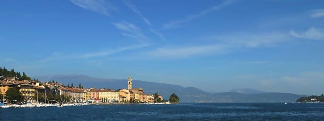Trip La Graciosa beliebte Urlaubsziele am Gardasee -  Mit einer Fläche von 370 km² ist der Gardasee der größte See Italiens. Es liegt am Fuße der Alpen und erstreckt sich über drei Staaten: Lombardei, Venetien und Trentino. Die maximale Tiefe des Sees beträgt 346 m, er hat eine längliche Form und sein nördliches Ende ist sehr schmal. Dort ist der See von den Bergen der Gruppo di Baldo umgeben. Du trittst aus deinem gemütlichen Hotelzimmer und es begrüßt dich die warme italienische Sonne. Du blickst auf den atemberaubenden Gardasee, der in zahlreichen Blautönen schimmert - von tiefem Dunkelblau bis zu funkelndem Türkis. Majestätische Berge umgeben dich, während die Brise sanft deine Haut streichelt und der Duft von blühenden Zitronenbäumen deine Nase kitzelt. Du schlenderst die malerischen, engen Gassen entlang, vorbei an farbenfrohen, blumengeschmückten Häusern. Vereinzelt unterbricht das fröhliche Lachen der Einheimischen die friedvolle Stille. Du fühlst dich wie in einem Traum, der nicht enden will. Jeder Schritt führt dich zu neuen Entdeckungen und Abenteuern. Du probierst die köstliche italienische Küche mit ihren frischen Zutaten und verführerischen Aromen. Die Sonne geht langsam unter und taucht den Himmel in ein leuchtendes Orange-rot - ein spektakulärer Anblick.